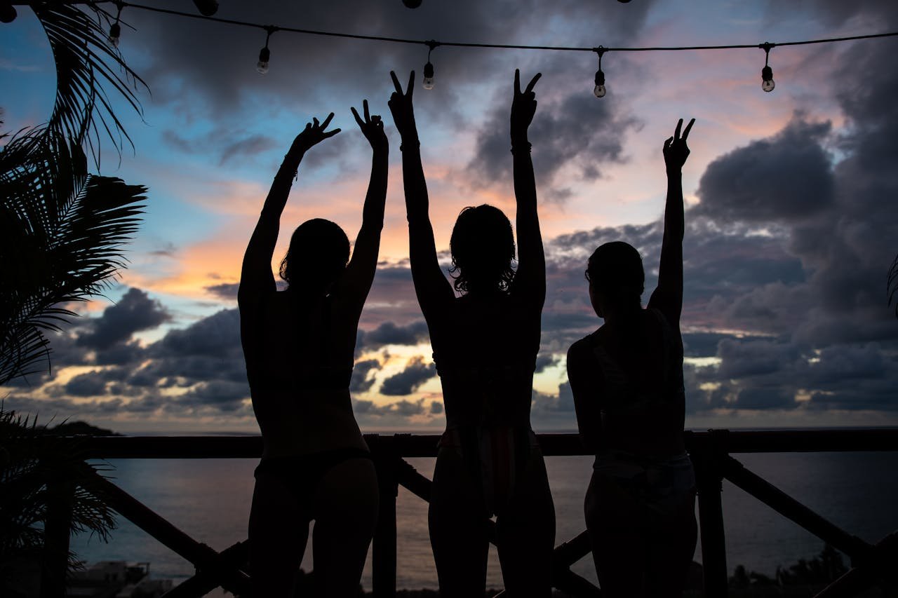 Three women silhouetted against a vibrant sunset, raising hands in victory.